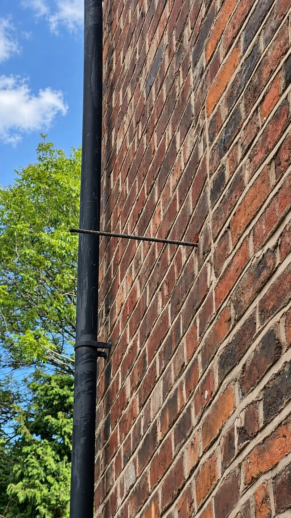 Network cable clipped along a mortar line on a brick wall, beside a black downpipe